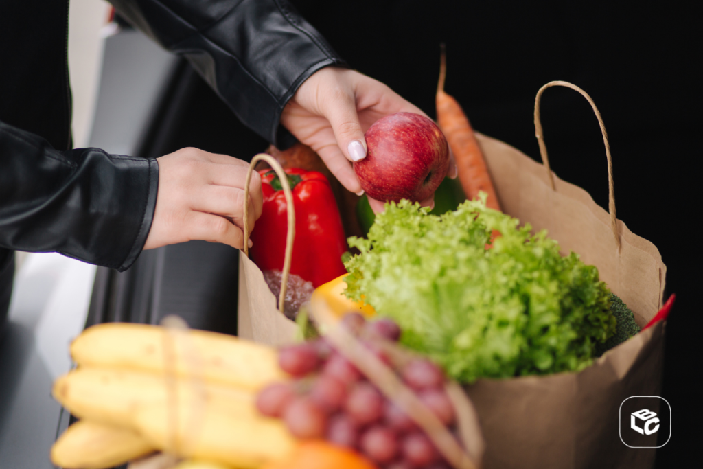 Mãos organizando sacola de compras com frutas e vegetais frescos.