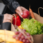 Mãos organizando sacola de compras com frutas e vegetais frescos.