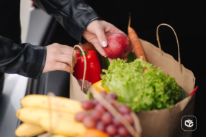Mãos organizando sacola de compras com frutas e vegetais frescos.